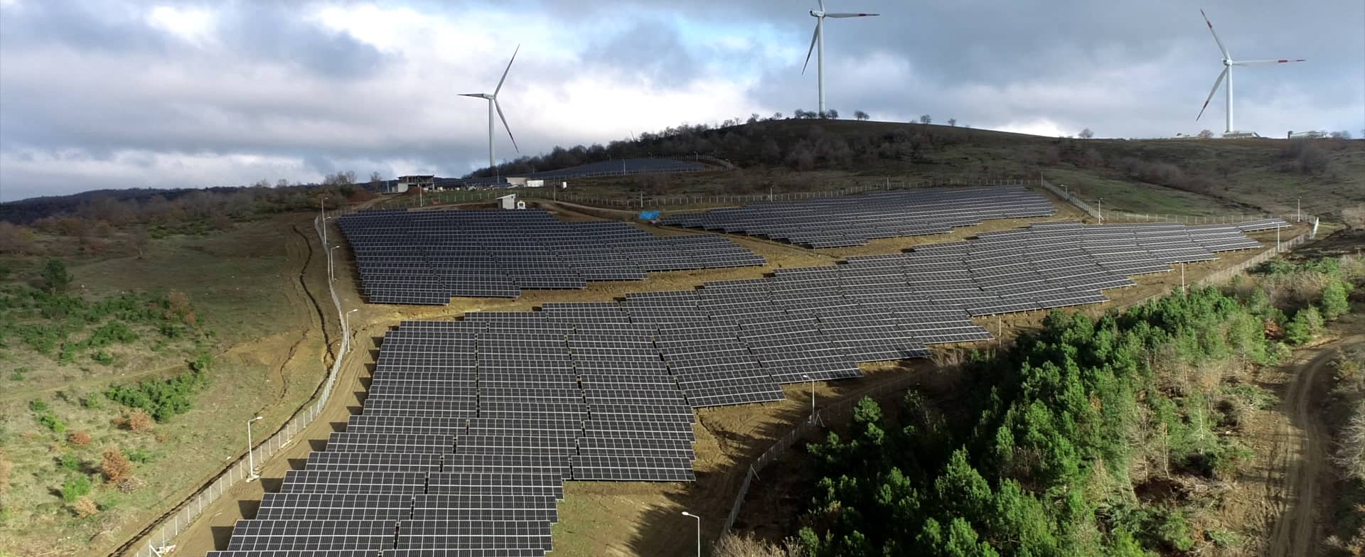 Artı Enerji’s Karacabey solar plant: rows of photovoltaic panels on a hillside, with wind turbines behind.