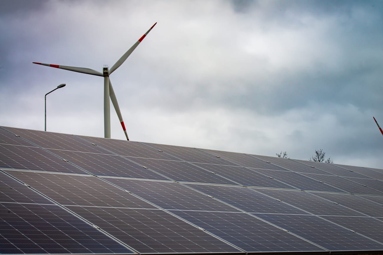 A wind turbine rising behind rows of solar panels.